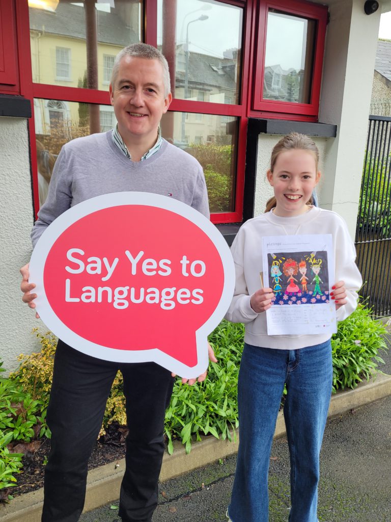Man holding a sign that says Say Yes to Languages, child holding a picture she drew.